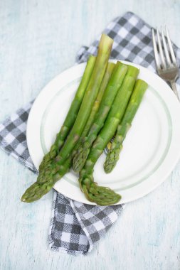Beyaz tabakta taze yeşil kuşkonmaz, peçete ve çatal, sağlıklı mevsimlik yiyecek kavramı.