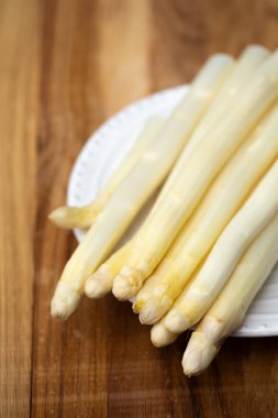 Sıcak ahşap zemin üzerine seramik tabakta taze beyaz kuşkonmaz mevsimsel organik üretim kavramı.