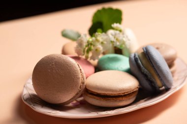 Bej bir arka planda pembe bir tabakta çiçek desenli farklı dolgulu kurabiyeler.