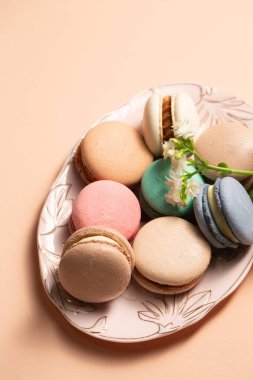 Bej bir arka planda pembe bir tabakta çiçek desenli farklı dolgulu kurabiyeler.