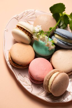 Bej bir arka planda pembe bir tabakta çiçek desenli farklı dolgulu kurabiyeler.