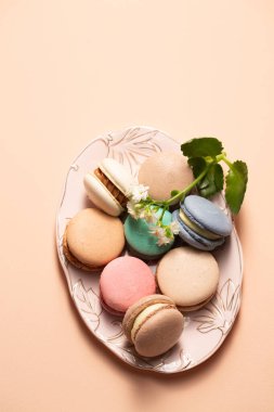 Bej bir arka planda pembe bir tabakta çiçek desenli farklı dolgulu kurabiyeler.