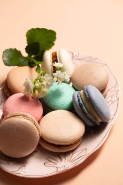 Bej bir arka planda pembe bir tabakta çiçek desenli farklı dolgulu kurabiyeler.