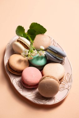 Bej bir arka planda pembe bir tabakta çiçek desenli farklı dolgulu kurabiyeler.