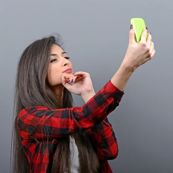 Portrait of a girl taking selfie with cellphone against gray bac — Stock Photo, Image