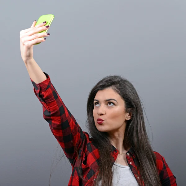 灰色の bac に対して携帯電話で selfie を取っている女の子の肖像画 — ストック写真