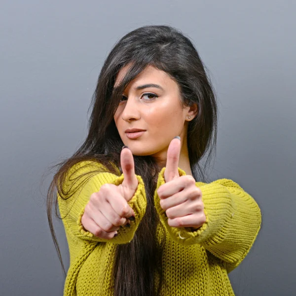 Portrait of happy woman holding thumbs up against gray backgroun — Stok Foto