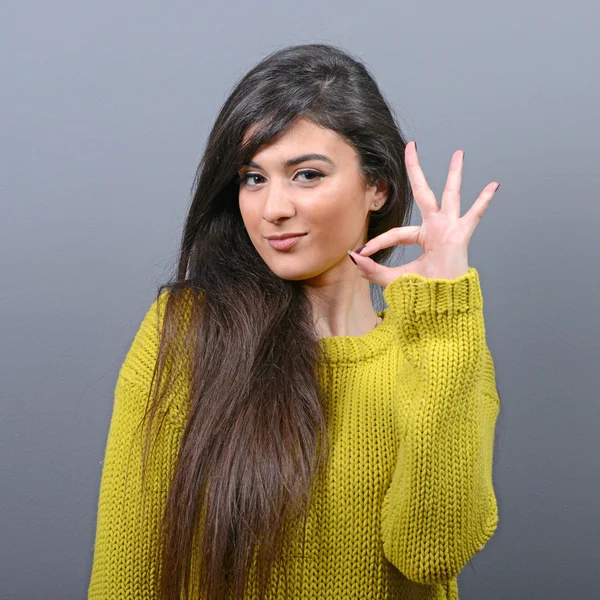 Portrait of happy woman showing ok sign against gray background — Stock Photo, Image