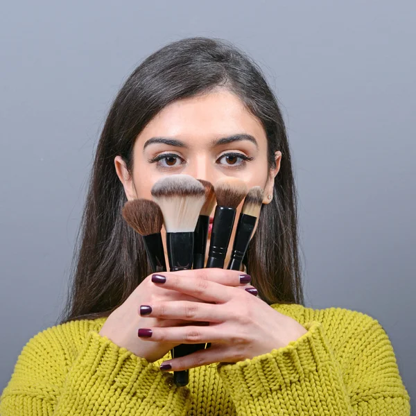 Portrait de femme tenant des pinceaux de maquillage sur fond gris — Photo