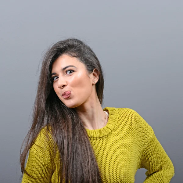 Retrato de mujer sobresaliendo de su lengua contra fondo gris — Foto de Stock