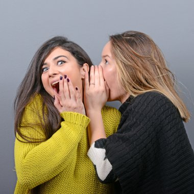 Gri bir arka plana dayanır sırları fısıldayan iki kadın arkadaş