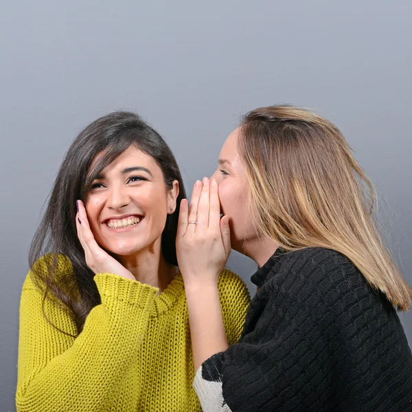 Zwei Freundinnen flüstern Geheimnisse vor grauem Hintergrund — Stockfoto