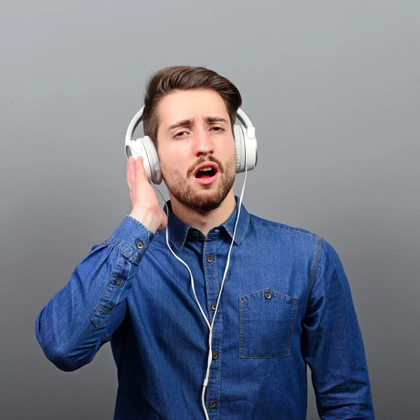 Young man leaned on the wall enjoying music against gray backgro — Stock Photo, Image