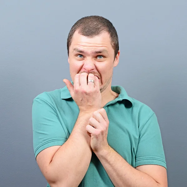 Portret mężczyzny gryzienie paznokci i trwający przestraszony wobec szary bac — Zdjęcie stockowe