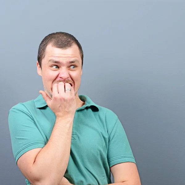 Portrait of a man biting nails and being scared against gray bac — Stock Photo, Image