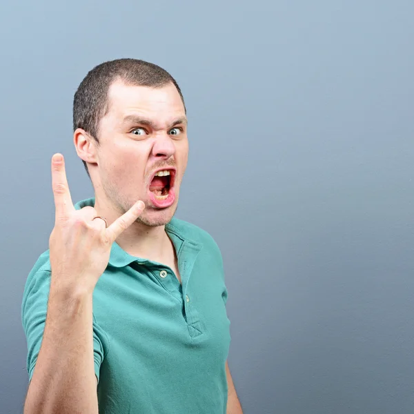 Retrato de um homem mostrando gesto de rocha contra fundo cinza — Fotografia de Stock