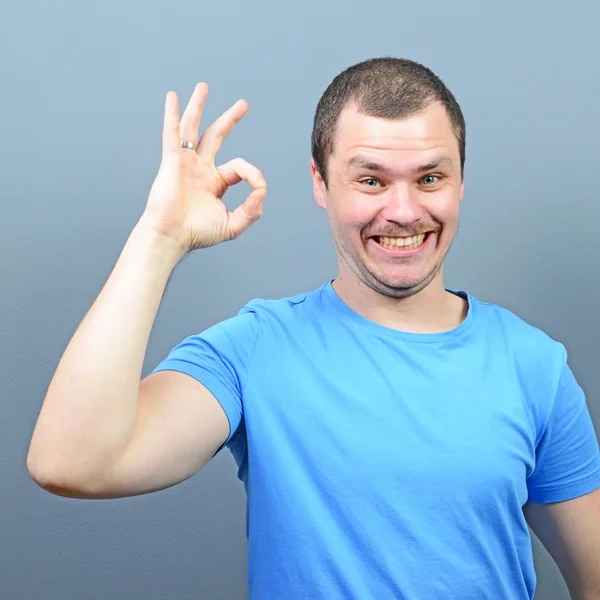 Retrato de un hombre mostrando el pulgar hacia arriba o signo de ok contra la espalda gris — Foto de Stock