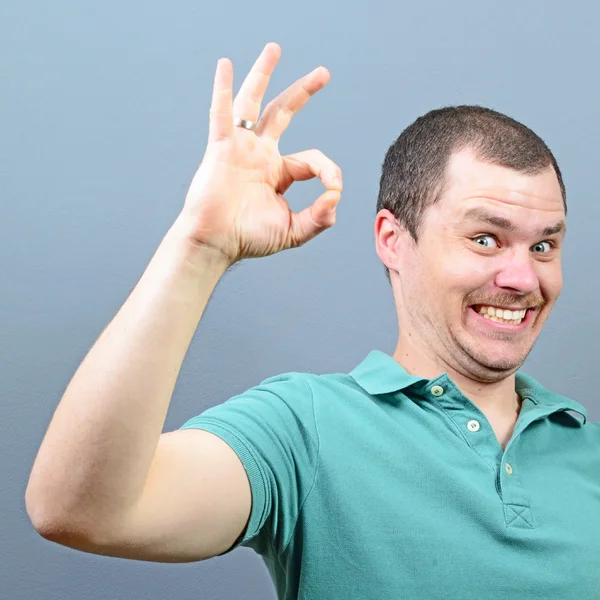 Portrait of a man showing thumb up or ok sign against gray backg — Stock Photo, Image