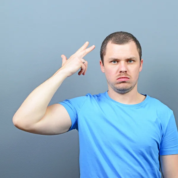 Portrait of man making gun gesture to the head against gray back — Stock Photo, Image