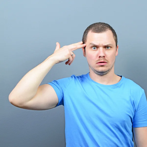 Retrato del hombre haciendo gesto de pistola en la cabeza contra la espalda gris —  Fotos de Stock