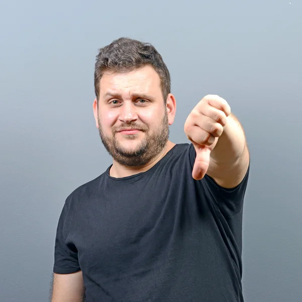 Portrait of chubby young man showing thumb down against gray bac — Stock Photo, Image