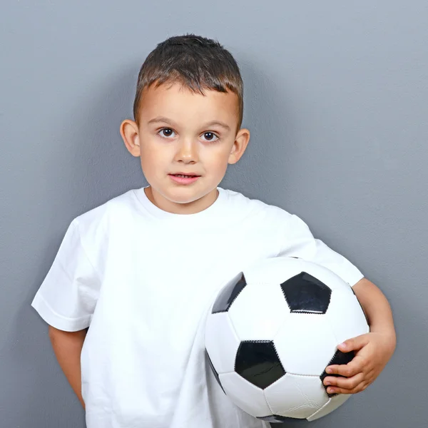 Симпатичный маленький мальчик позирует с футболом на сером фоне — стоковое фото