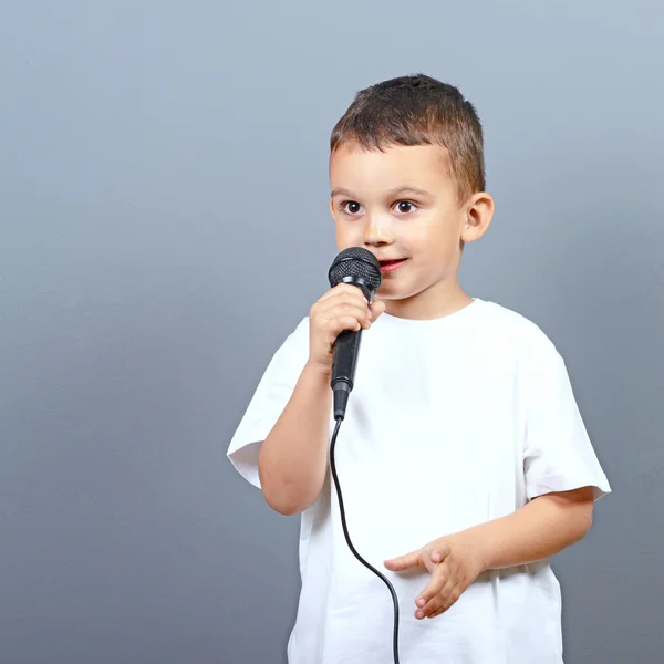 Schattige kleine jongen jongen zingen op microfoon tegen de grijze pagina — Stockfoto