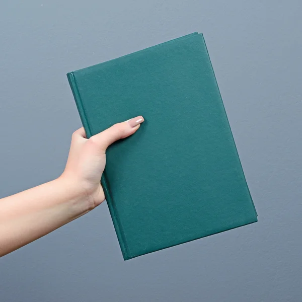 Рука держит зеленую книгу на сером фоне — стоковое фото