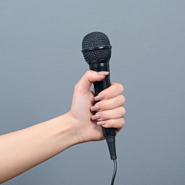 Hand holding microphone against gray background — Stock Photo, Image