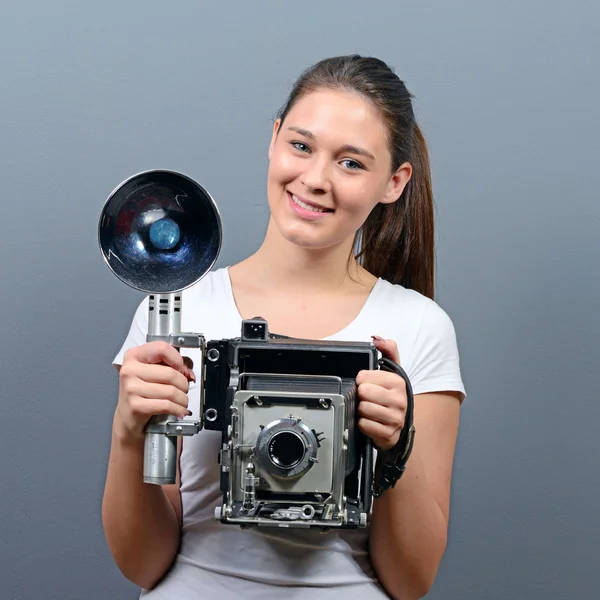 Retrato de una mujer joven sosteniendo cámara retro contra la espalda gris — Foto de Stock