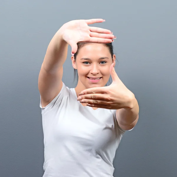 Portrait of a young woman making frame with hands against gray b — Stock Photo, Image