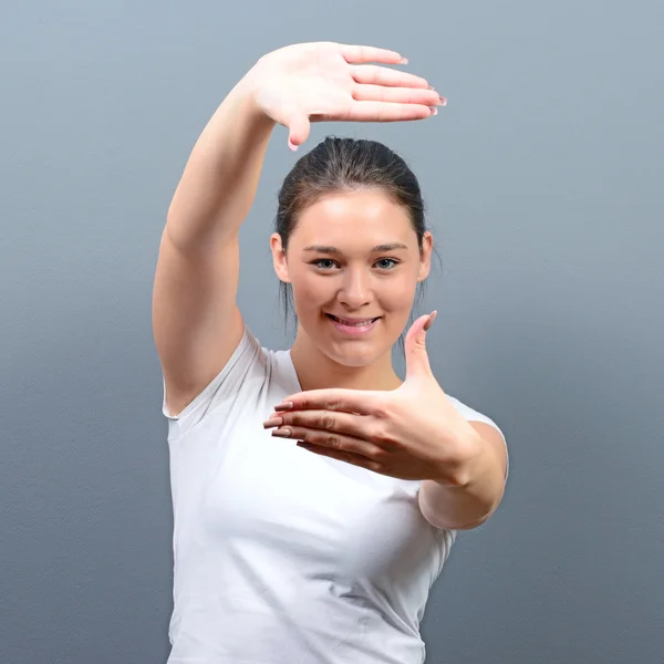 Retrato de una mujer joven haciendo marco con las manos contra gris b — Foto de Stock