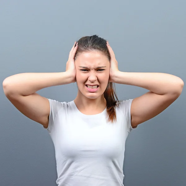 Portrait of woman covering ears with hands against gray backgrou — Stock Photo, Image