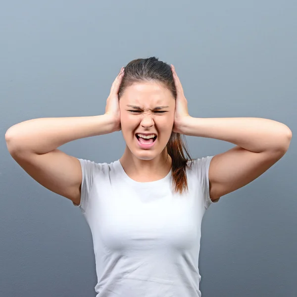 Portrait of woman covering ears with hands against gray backgrou — Stock Photo, Image