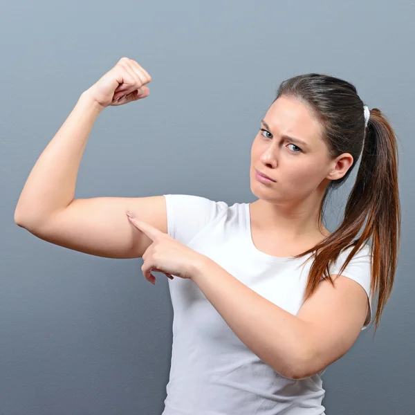 Pretty young brunette woman showing bicep on her arm against gra — Stock Photo, Image