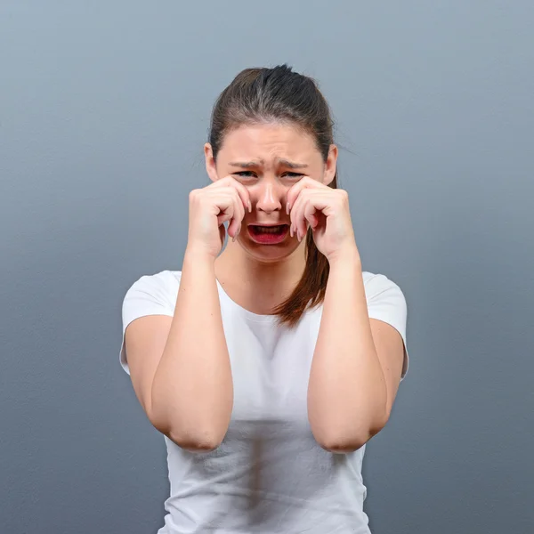Mulher chorando e enxugando lágrimas contra fundo cinza — Fotografia de Stock