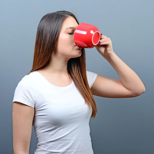 Woman drinking hot beverage against gray background — Stock Photo, Image