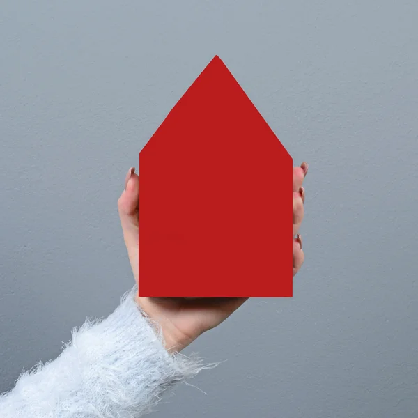 Junge Frau hält Haus vor grauem Hintergrund - Immobilien — Stockfoto