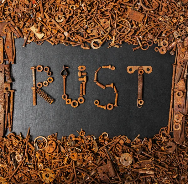 RUST made with rusty screws and bolts on black board with frame — Stock Photo, Image