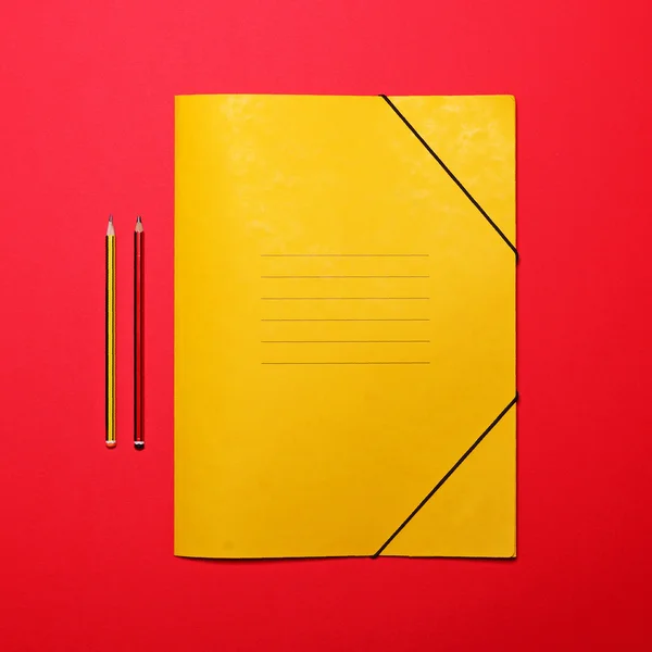 Tom gul mapp på röd bakgrund med pennor - platt låg mi — Stockfoto