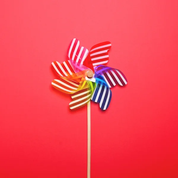 Pinwheel multicolorido contra fundo vermelho - Pavilhão plano mínimo — Fotografia de Stock
