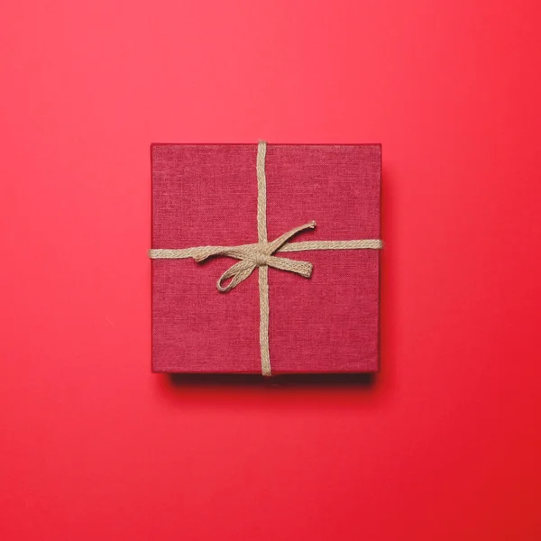 Red gift box with rope bow on red background - Minimal design — Stock Photo, Image