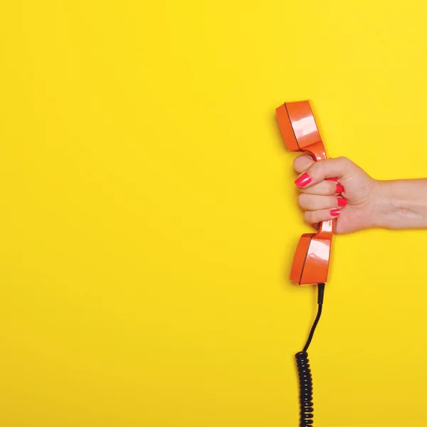 Mulher mão segurando retro tubo de telefone laranja contra backgr amarelo — Fotografia de Stock