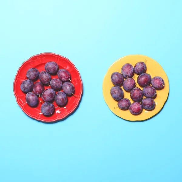 Top view of fresh plums in yellow and red plate on blue backgrou — Stock Photo, Image