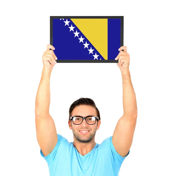 Portrait of a young casual man holding up board with National fl — Stock Photo, Image