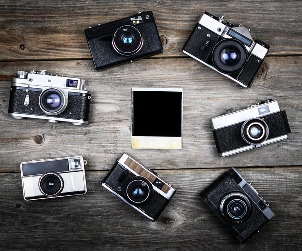 Группа винтажных камер вокруг одной пустой фотографии на деревянном фоне — стоковое фото