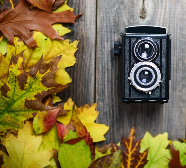 Retro fotoaparát na dřevěný stůl s podzimní listí — Stock fotografie