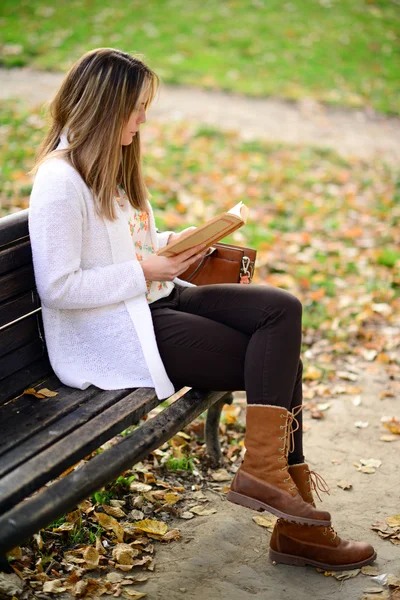Woman reading a book at bench in autumn park — Stock Photo, Image