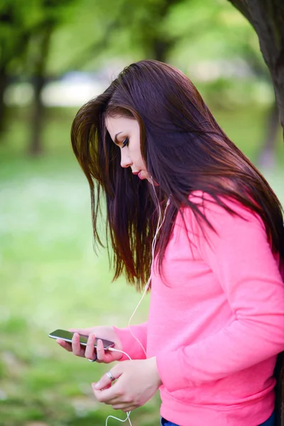 Female student girl outside in park listening to music on headphones — Stock Photo, Image