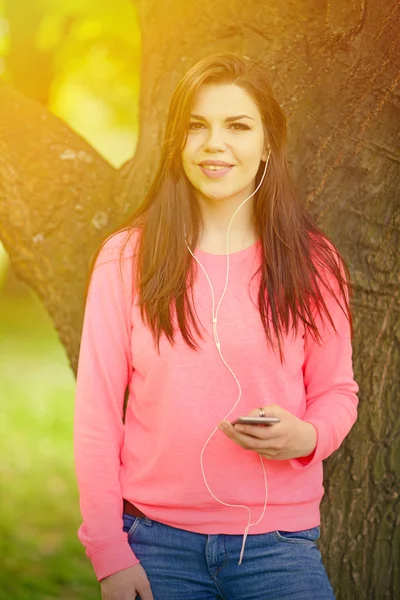 Девушка-студентка на улице в парке слушает музыку на хедф — стоковое фото